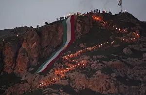 Images Dated 20th March 2014: Iraqi Kurdish people carry fire torches up a mountain where a giant flag of Iraq s