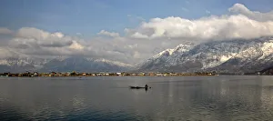 Kashmiri man rows boat on Dal Lake surrounded by snow-covered mountains in Srinagar Kashmiri man rows boat on Dal Lake surrounded by snow-covered mountains in Srinagar