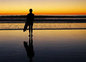 A lone surfer stands watching the waves after surfing as the sun sets in Leucadia A lone surfer stands watching the waves after surfing as the sun sets in Leucadia