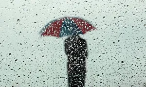 A man carrying an umbrella is seen silhouetted through a window covered with rain drops A man carrying an umbrella is seen silhouetted through a window covered with rain drops
