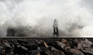A man is drenched by a large wave during high tide as he cycles past at a fishing A man is drenched by a large wave during high tide as he cycles past at a fishing