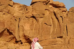 Man looks at a camel sculpture carved on a rock in Al-Jouf
