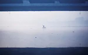 A man paddles a handmade boat across the Yamuna river on a foggy winter morning in A man paddles a handmade boat across the Yamuna river on a foggy winter morning in
