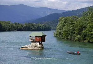 Images Dated 22nd May 2013: A man powers a boat near a house built on a rock on the river Drina near the western