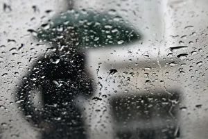 A man is seen through raindrops on a window as he shelters under an umbrella in central A man is seen through raindrops on a window as he shelters under an umbrella in central