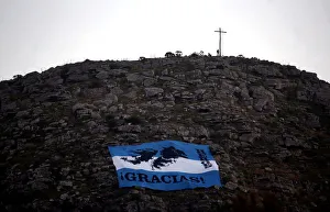 A man stands next to a cross as an Argentine national flag with an image of the Falkland A man stands next to a cross as an Argentine national flag with an image of the Falkland