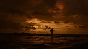 Gold Colour Gallery: A man stands in the sea with his hands on his hips as he watches the sunset in Hikkaduwa