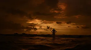 A man stands in the sea with his hands on his hips as he watches the sunset in Hikkaduwa A man stands in the sea with his hands on his hips as he watches the sunset in Hikkaduwa