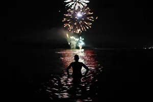 Firework Gallery: A man watches fireworks as he takes a bath in the Mediterranean Sea on San Juans night