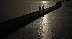 Men are silhouetted against the setting sun as they walk by the sea in Karachi Men are silhouetted against the setting sun as they walk by the sea in Karachi