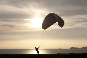 A paragliding instructor arranges his paraglide at the ocean-front in the neighbourhood A paragliding instructor arranges his paraglide at the ocean-front in the neighbourhood