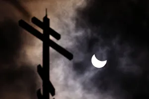 A partial solar eclipse forms in the sky through clouds near the cross of the Church of A partial solar eclipse forms in the sky through clouds near the cross of the Church of
