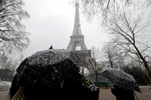 People use umbrellas to take cover from falling snow near the Eiffel Tower in Paris