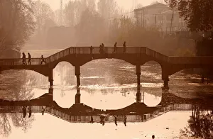 People walk on a wooden footbridge across a canal during an autumn day in Srinagar People walk on a wooden footbridge across a canal during an autumn day in Srinagar