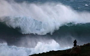 A photographer takes pictures of waves breaking on the Brittany coast at Audierne in