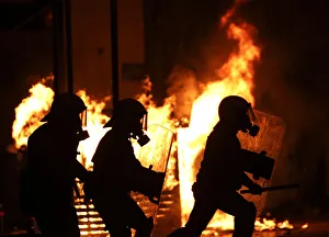 Riot policemen are silhouetted as they run in front of a burning kiosk during clashes in Riot policemen are silhouetted as they run in front of a burning kiosk during clashes in