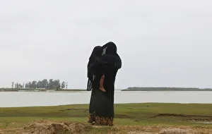 A Rohingya refugee woman protects her son from rain as she looks towards the beach after A Rohingya refugee woman protects her son from rain as she looks towards the beach after