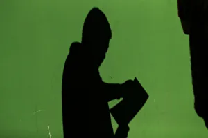 The shadow of a man is cast on a wall as he checks his documents after leaving a The shadow of a man is cast on a wall as he checks his documents after leaving a