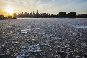 The sun sets behind the Manhattan skyline as ice floats down the East River in New York The sun sets behind the Manhattan skyline as ice floats down the East River in New York