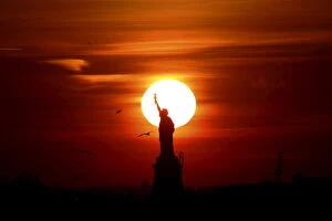 Images Dated 28th February 2016: The sun sets behind the Statue of Liberty in New Yorks Harbor as seen from the Brooklyn