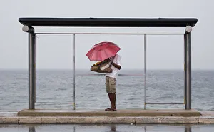 A vendor holds up an umbrella as he seeks shelter from the heavy rain under a bus stand A vendor holds up an umbrella as he seeks shelter from the heavy rain under a bus stand