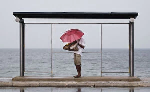 Images Dated 2nd November 2013: A vendor holds up an umbrella as he seeks shelter from the heavy rain under a bus stand