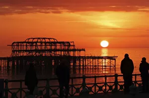 Images Dated 16th February 2013: Visitors watch the sun set behind the remains of the West Pier on the seafront at Brighton