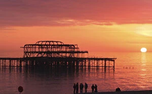 Images Dated 16th February 2013: Visitors watch the sun set behind the remains of the West Pier on the seafront at Brighton