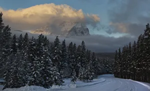 A winding hillside road is seen with a mountain covered in low clouds inside Banff A winding hillside road is seen with a mountain covered in low clouds inside Banff