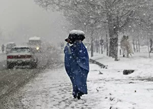 Images Dated 11th February 2012: A woman carries a sack on her head along a street on a snowy day in Kabul