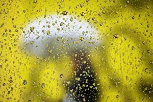 A woman carrying an umbrella is pictured from behind a car window covered with rain A woman carrying an umbrella is pictured from behind a car window covered with rain
