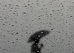 A woman carrying an umbrella is silhouetted from behind a window covered with rain drops A woman carrying an umbrella is silhouetted from behind a window covered with rain drops