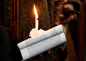 A woman holds a candle and the Bible during the Orthodox Christmas mass at the St A woman holds a candle and the Bible during the Orthodox Christmas mass at the St