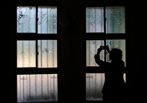 A woman uses her mobile phone to take pictures of bullet holes in windows damaged during A woman uses her mobile phone to take pictures of bullet holes in windows damaged during
