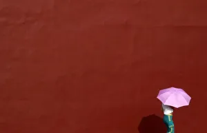 A woman uses an umbrella to shade herself from the sun as she walks next to a wall A woman uses an umbrella to shade herself from the sun as she walks next to a wall