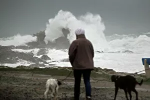 A woman walks her dogs as waves break on the Brittany coast after storm Eleanor hit