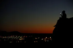 A young couple look at their phone as they sit on a hillside after sun set in El Paso A young couple look at their phone as they sit on a hillside after sun set in El Paso