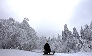 A young girl sits on her sledge on top of the Feldberg mountain during a winter day A young girl sits on her sledge on top of the Feldberg mountain during a winter day