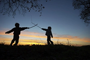 Young children playing having a stick fight on edge of woodland at sunset Norfolk Young children playing having a stick fight on edge of woodland at sunset Norfolk