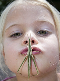 Africa, Kenya. Young girl puckers up with grasshopper on her mouth. (MR) Africa, Kenya. Young girl puckers up with grasshopper on her mouth. (MR)