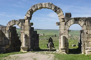 Africa, Morocco. A man on a donkey passes under stone columns and arches at the roman Africa, Morocco. A man on a donkey passes under stone columns and arches at the roman