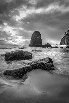 Black and white vertical of swirling water around rocks on a beach Black and white vertical of swirling water around rocks on a beach