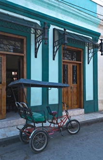 Camaquey Cuba street scene of old bike carriage on street and buildings Camaquey Cuba street scene of old bike carriage on street and buildings