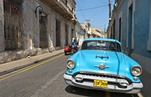 Camaquey Cuba street scene of old Oldsmobile car on street and buildings Camaquey Cuba street scene of old Oldsmobile car on street and buildings