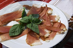 Dried dry cured ham with basil leaves on a white plate. Tradita traditional restaurant Dried dry cured ham with basil leaves on a white plate. Tradita traditional restaurant