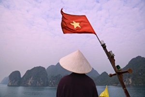 Girl with conical hat on a junk boat with national flag and karst islands in Halong Bay Girl with conical hat on a junk boat with national flag and karst islands in Halong Bay