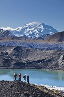 A group of hikers stand on moraine next to a glacial meltpond at the edge of the Muldrow Glacier A group of hikers stand on moraine next to a glacial meltpond at the edge of the Muldrow Glacier