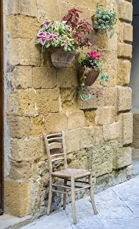 Italy, Tuscany. Chair and flower pots outside the entrance to a shop in a village in Italy, Tuscany. Chair and flower pots outside the entrance to a shop in a village in