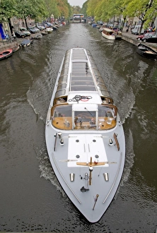 A long glass topped tour boattravels down a boat lined canal A long glass topped tour boattravels down a boat lined canal