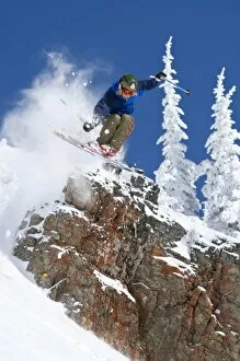 Down Hill Gallery: Man jumping colorful cliff and skiing in fresh powder at Whitefish Mountain Resort in Montana